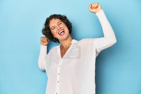 Foto de Joven mujer caucásica con el pelo corto celebrando un día especial, salta y levanta los brazos con energía. - Imagen libre de derechos