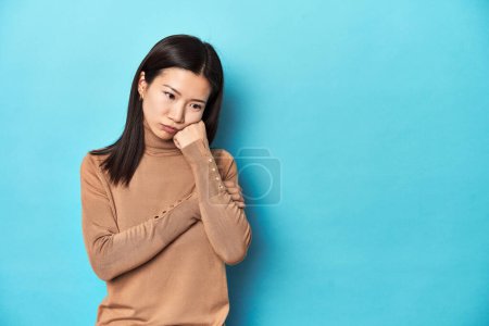 Téléchargez les photos : Jeune femme asiatique au col roulé marron, qui se sent triste et onéreux, regardant l'espace de copie. - en image libre de droit