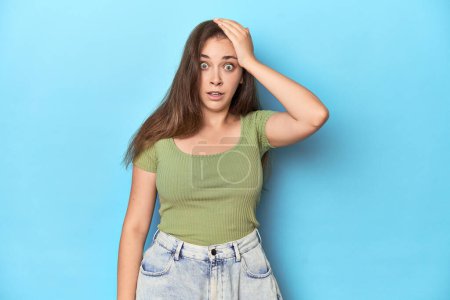 Photo for Young Caucasian woman in a green top on a blue backdrop being shocked, she has remembered important meeting. - Royalty Free Image