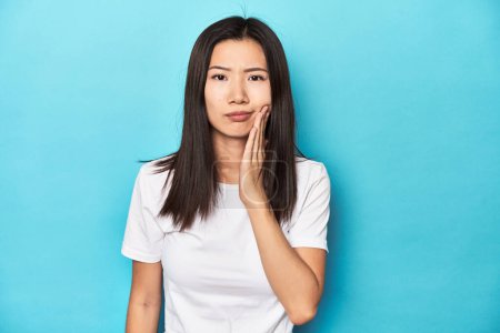 Foto de Mujer asiática joven en camiseta blanca, tiro al estudio, con un fuerte dolor de dientes, dolor molar. - Imagen libre de derechos