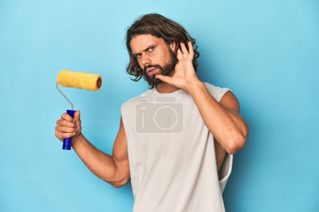 Téléchargez les photos : Homme barbu peignant avec un rouleau jaune essayant d'écouter un potins. - en image libre de droit