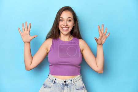 Téléchargez les photos : Jeune femme à la mode dans un haut violet sur fond bleu montrant le numéro dix avec les mains. - en image libre de droit
