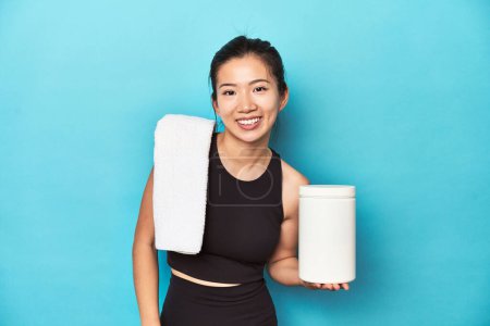 Photo for Young Asian sportswoman with protein bottle, gym setup, laughing and having fun. - Royalty Free Image