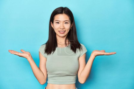 Téléchargez les photos : Femme asiatique en haut vert d'été, toile de fond studio, fait échelle avec les bras, se sent heureux et confiant. - en image libre de droit