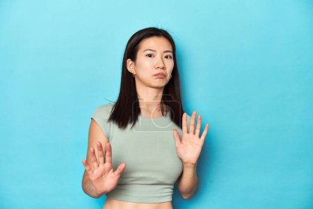 Photo for Asian woman in summer green top, studio backdrop, rejecting someone showing a gesture of disgust. - Royalty Free Image