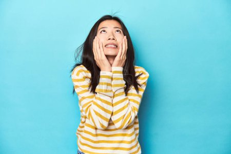 Photo for Asian woman in striped yellow sweater, whining and crying disconsolately. - Royalty Free Image