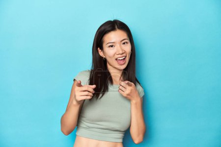 Téléchargez les photos : Femme asiatique en haut vert d'été, toile de fond studio, pointant vers l'avant avec les doigts. - en image libre de droit