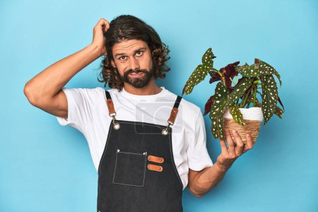 Photo for Long-haired gardener with beard holding a plant being shocked, she has remembered important meeting. - Royalty Free Image