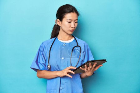 Téléchargez les photos : Asiatique infirmière avec tablette, examen d'un rapport, plan studio. - en image libre de droit