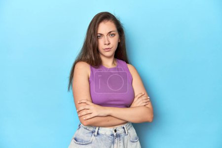 Photo for Fashionable young woman in a purple top on blue background suspicious, uncertain, examining you. - Royalty Free Image
