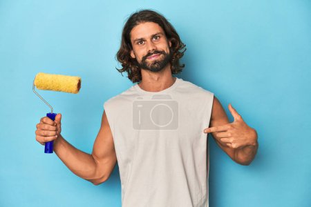 Téléchargez les photos : Peinture homme barbu avec une personne rouleau jaune pointant à la main vers un espace de copie chemise, fier et confiant - en image libre de droit