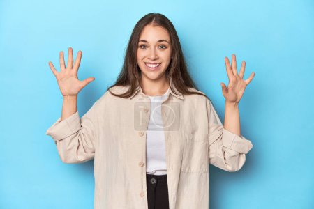Foto de Mujer joven con estilo en una camiseta sobre un fondo azul que muestra el número diez con las manos. - Imagen libre de derechos