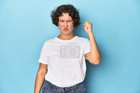 Photo for Young Caucasian woman with short hair showing fist to camera, aggressive facial expression. - Royalty Free Image
