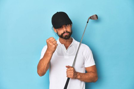 Foto de Golfista de pelo largo con club y sombrero mostrando puño a cámara, expresión facial agresiva. - Imagen libre de derechos