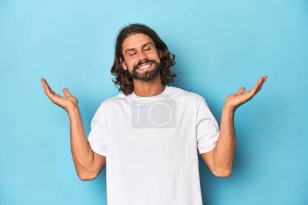 Téléchargez les photos : Homme barbu en chemise blanche, fond bleu joyeux riant beaucoup. Concept de bonheur. - en image libre de droit