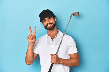 Téléchargez les photos : Golfeur aux cheveux longs avec club et chapeau joyeux et insouciant montrant un symbole de paix avec les doigts. - en image libre de droit