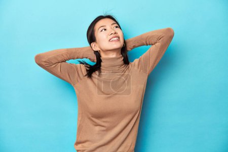 Téléchargez les photos : Jeune femme asiatique au col roulé marron, bras tendus, position détendue. - en image libre de droit