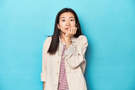 Téléchargez les photos : Femme asiatique en chemise à couches et t-shirt rayé, ongles mordants, nerveux et très anxieux. - en image libre de droit