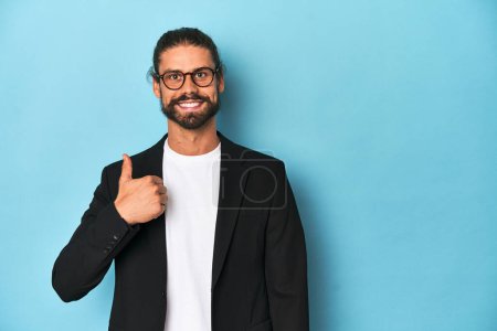 Téléchargez les photos : Homme d'affaires en costume avec lunettes et barbe souriant et levant le pouce - en image libre de droit