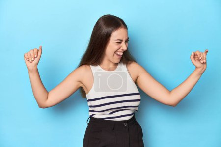 Photo for Woman in a striped top posing on a blue studio backdrop dancing and having fun. - Royalty Free Image