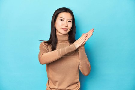 Photo for Young Asian woman in brown turtleneck, feeling energetic and comfortable, rubbing hands confident. - Royalty Free Image