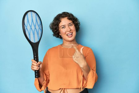Photo for Young woman with electric mosquito racket Young woman with electric mosquito racketpointing with finger at you as if inviting come closer. - Royalty Free Image
