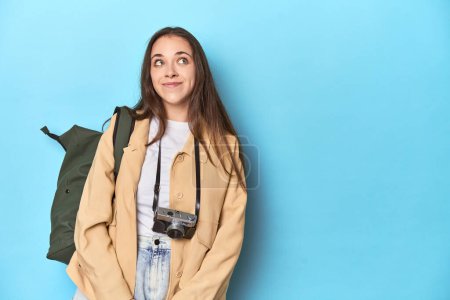 Photo for Young Caucasian woman traveler with camera and backpack dreaming of achieving goals and purposes - Royalty Free Image
