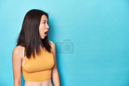 Photo for Asian woman in summer yellow top, studio setup, being shocked because of something she has seen. - Royalty Free Image