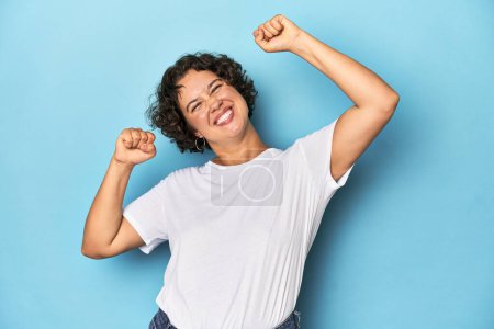 Foto de Joven mujer caucásica con el pelo corto celebrando un día especial, salta y levanta los brazos con energía. - Imagen libre de derechos