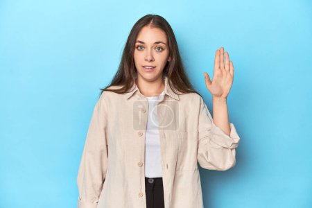 Téléchargez les photos : Jeune femme élégante dans un survêtement sur un fond bleu souriant gai montrant numéro cinq avec les doigts. - en image libre de droit