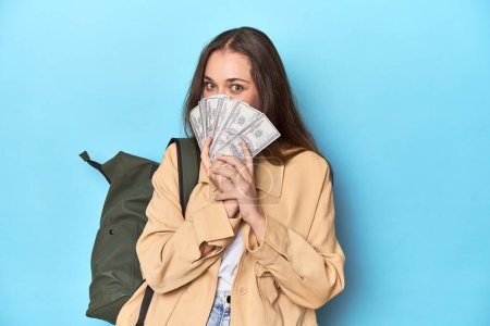 Photo for Traveling woman with backpack holding dollar bills on blue. - Royalty Free Image