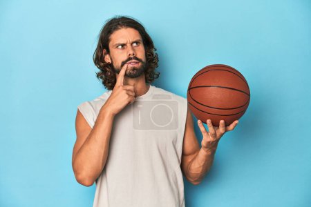Photo for Bearded man with basketball in blue studio relaxed thinking about something looking at a copy space. - Royalty Free Image