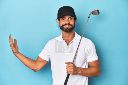 Foto de Golfista de pelo largo con club y sombrero recibiendo una agradable sorpresa, emocionado y levantando las manos. - Imagen libre de derechos