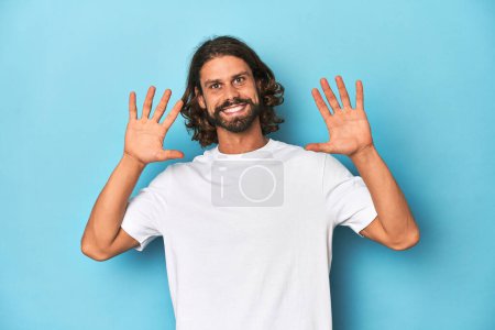 Téléchargez les photos : Homme barbu dans une chemise blanche, fond bleu montrant le numéro dix avec les mains. - en image libre de droit