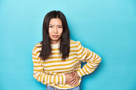 Téléchargez les photos : Femme asiatique en pull jaune rayé, ayant une douleur au foie, maux d'estomac. - en image libre de droit