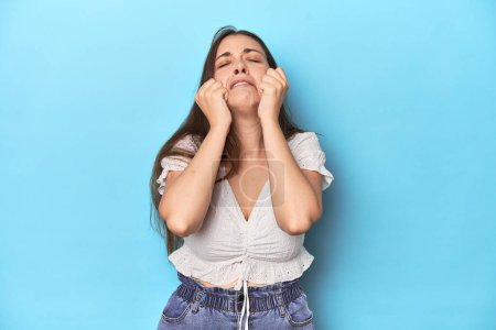 Photo for Stylish young woman in white blouse on a blue studio backdrop crying, unhappy with something, agony and confusion concept. - Royalty Free Image