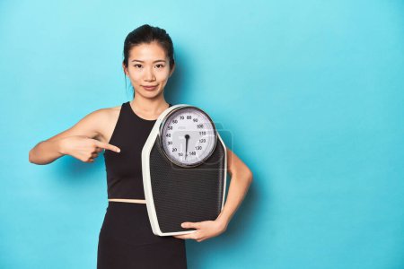 Photo for Asian sportswoman holding scale, studio shot. - Royalty Free Image