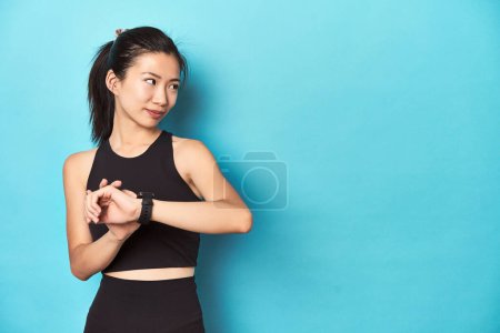 Photo for Asian sportswoman setting smartwatch before activity. - Royalty Free Image