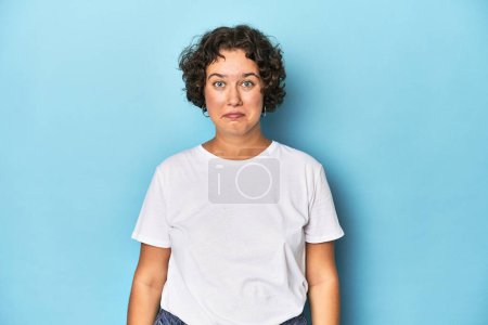 Foto de Mujer joven caucásica con pelo corto se encoge de hombros y los ojos abiertos confundidos. - Imagen libre de derechos