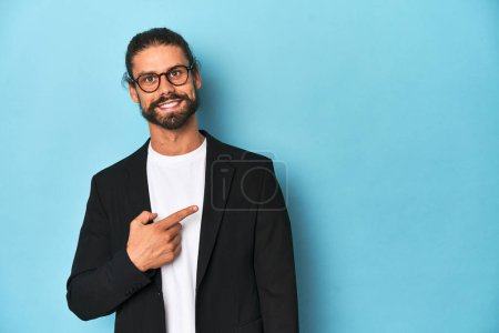 Foto de Empresario en traje con anteojos y barba sonriendo y señalando a un lado, mostrando algo en espacio en blanco. - Imagen libre de derechos