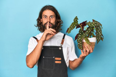 Foto de Jardinero de pelo largo con barba sosteniendo una planta guardando un secreto o pidiendo silencio. - Imagen libre de derechos
