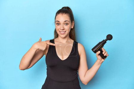 Photo for Active woman with an electric massager in a blue studio person pointing by hand to a shirt copy space, proud and confident - Royalty Free Image