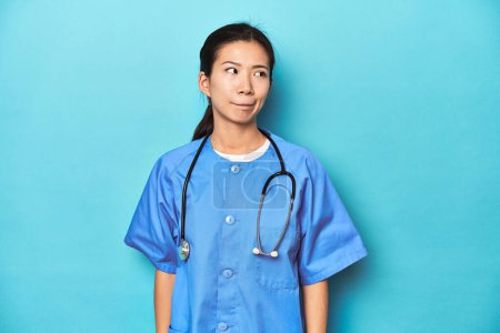 Téléchargez les photos : Infirmière asiatique avec stéthoscope, studio médical tourné, confus, se sent douteux et incertain. - en image libre de droit