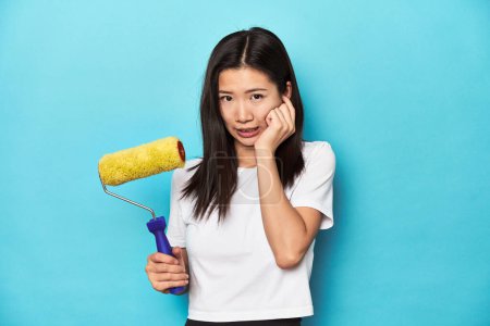 Téléchargez les photos : Jeune femme asiatique avec rouleau de peinture, concept de bricolage, couvrant les oreilles avec les mains. - en image libre de droit