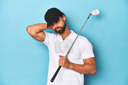 Foto de Golfista de pelo largo con club y sombrero tocando la parte posterior de la cabeza, pensando y haciendo una elección. - Imagen libre de derechos