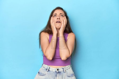 Photo for Fashionable young woman in a purple top on blue background whining and crying disconsolately. - Royalty Free Image