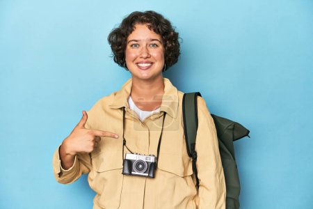 Téléchargez les photos : Jeune voyageuse avec caméra vintage personne pointant à la main vers un espace de copie de chemise, fière et confiante - en image libre de droit