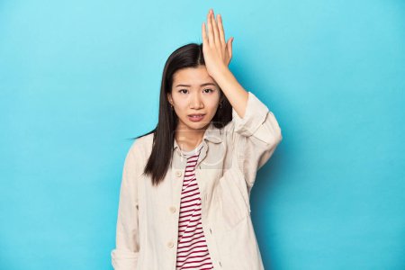 Photo for Asian woman in layered shirt and striped t-shirt, forgetting something, slapping forehead with palm and closing eyes. - Royalty Free Image