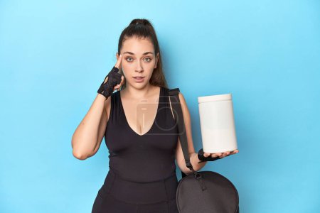 Photo for Young woman holding protein bottle in sporty setting pointing temple with finger, thinking, focused on a task. - Royalty Free Image