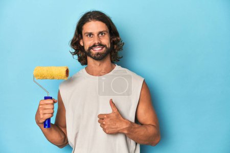 Photo for Bearded man painting with a yellow roller smiling and raising thumb up - Royalty Free Image